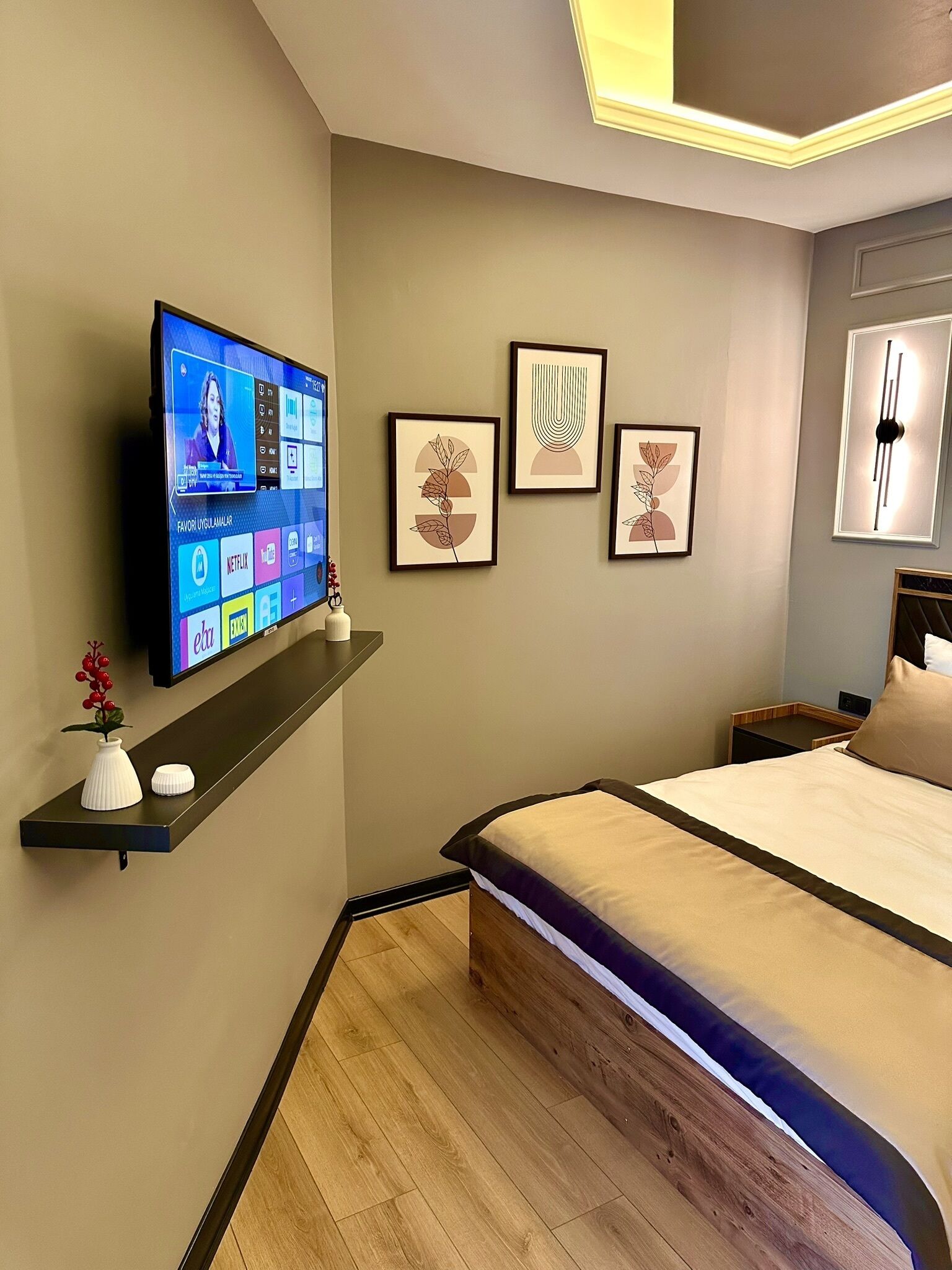 Une chambre à coucher moderne avec un lit, un téléviseur fixé au mur et des œuvres d’art encadrées accrochées au mur.