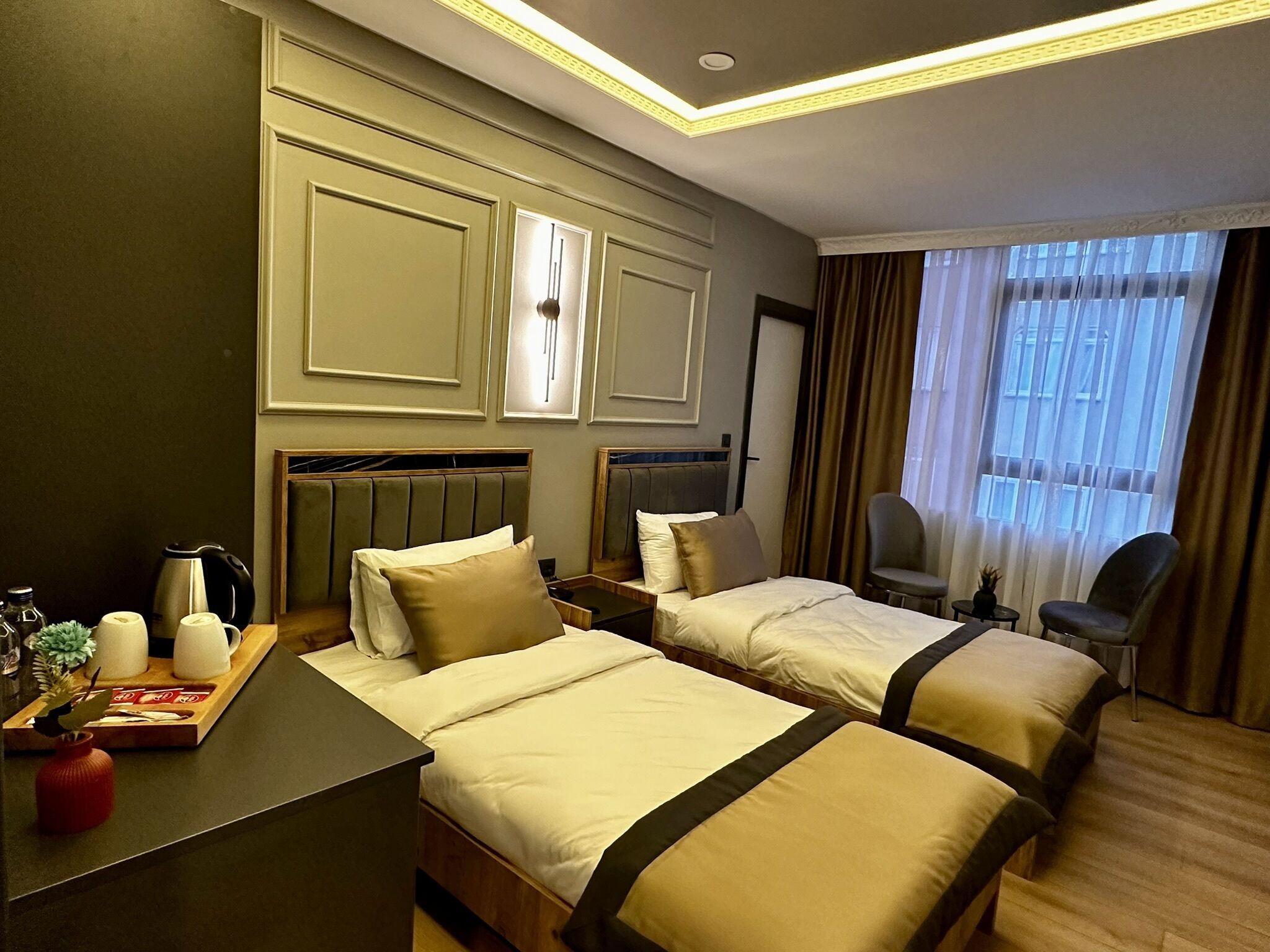 A hotel room with two beds, a desk, a chair, and a window with curtains.
