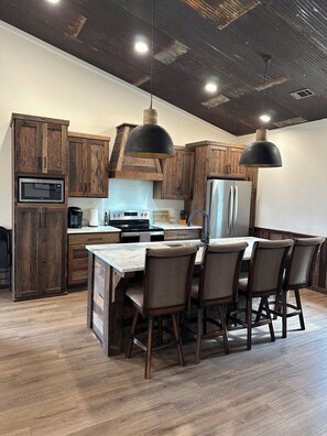 A modern kitchen with wooden cabinets, a central island with bar stools, a built-in microwave, and pendant lighting.