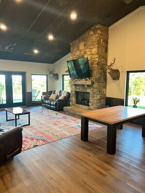 A spacious living room with a stone fireplace, leather furniture, and a mounted deer head.