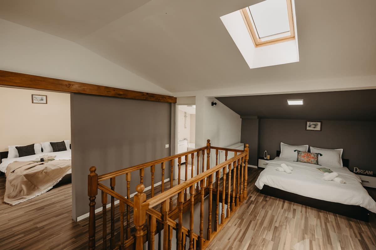 A bedroom with a wooden staircase, a skylight, and a large bed with white bedding.