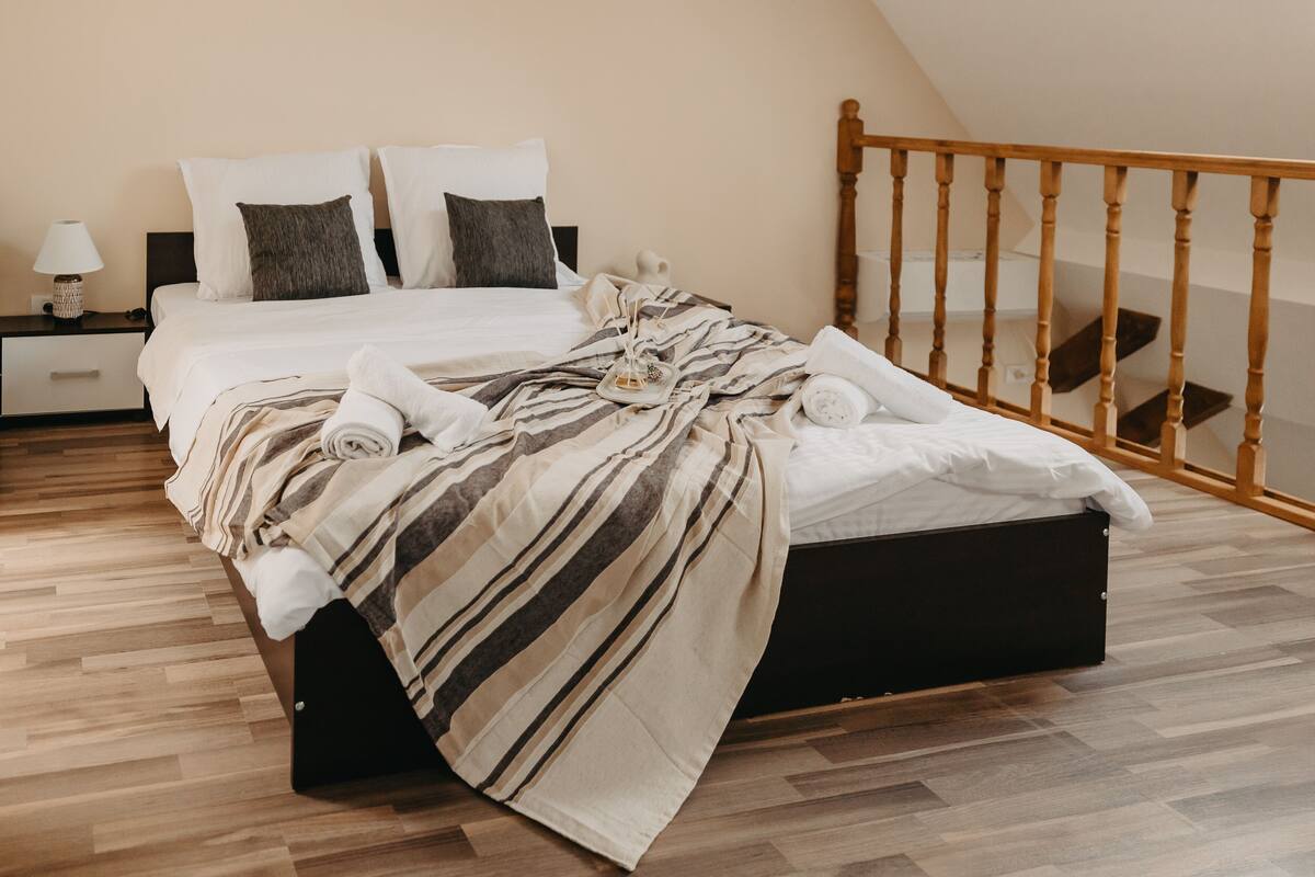 A neatly made bed with striped bedding, a bedside table with a lamp, and a wooden headboard.