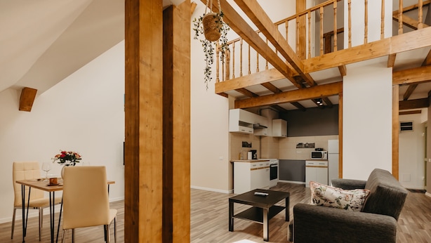 A spacious living area with a wooden staircase, a dining table with chairs, and a kitchen in the background. - Agoston Galgon Holiday Apartments (Timisoara)