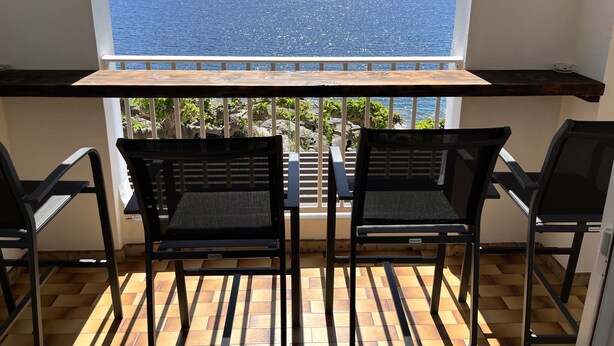 A balcony with two black chairs and a wooden table, overlooking a clear blue sea and distant mountains. - Appartement à Tiuccia, les Pieds Dans L'eau, Climatisé, Wifi (Tiuccia)