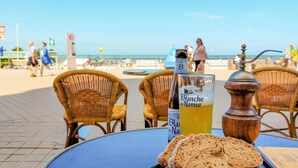 A table with a drink, a bottle, and a piece of bread on a beachside setting.