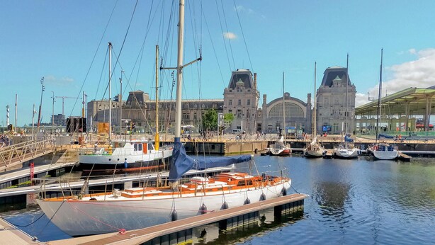 A marina with boats docked, a large building with a clock tower, and a covered walkway.