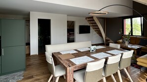 A spacious loft with a high ceiling, a dining area with a wooden table and chairs, a staircase, and a cozy seating area with a sofa and a coffee table.
