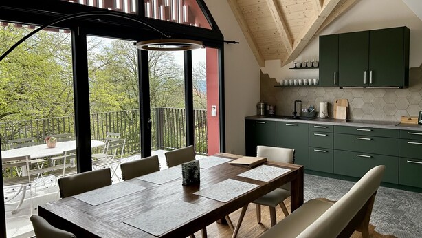 A modern kitchen with green cabinets, a wooden dining table with chairs, and a view of the outdoors.