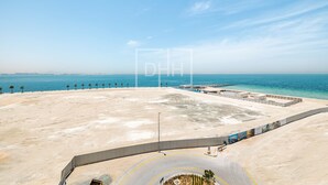 An aerial view of a coastal area with a sandy beach, a curved road, and a water body. - Full Sea View 1Bed Le Pont B1 in La Mer (Dubai)