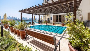 A rooftop pool with a pergola, potted plants, and a bench. - Full Sea View 1Bed Le Pont B1 in La Mer (Dubai)
