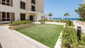 A modern building with a flat roof, a courtyard with artificial grass, and a view of the sea. - Full Sea View 1Bed Le Pont B1 in La Mer (Dubai)