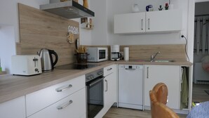 A modern kitchen with white cabinets, a wooden countertop, a toaster, a kettle, a microwave, a coffee maker, and a dishwasher.