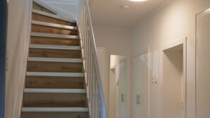 A staircase with wooden steps and white railings, leading to a landing with a light fixture.