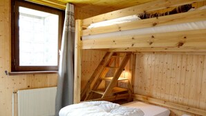 A wooden cabin room with bunk beds, a window with curtains, and a radiator.