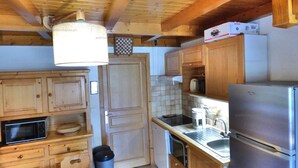A compact kitchen with wooden cabinets, a stainless steel refrigerator, a microwave, and a sink.