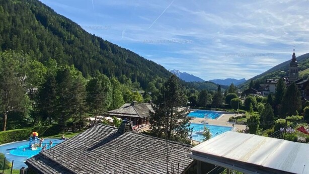 A resort with a swimming pool, a mountain backdrop, and a church spire.