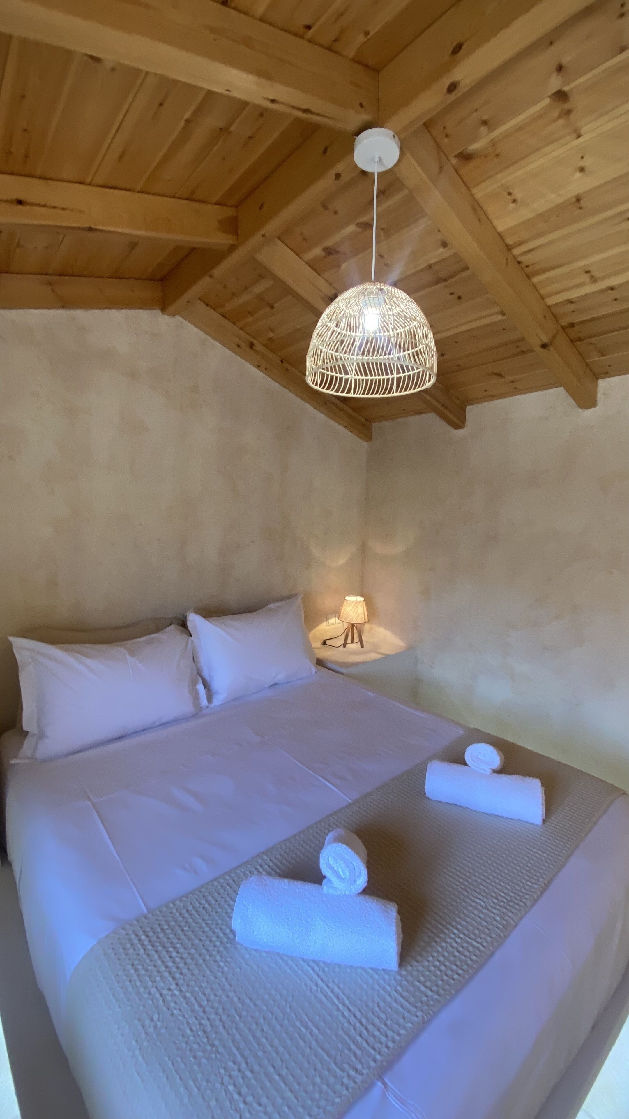 A bedroom with a wooden ceiling, a bed with white bedding, a hanging light fixture, and a bedside lamp.