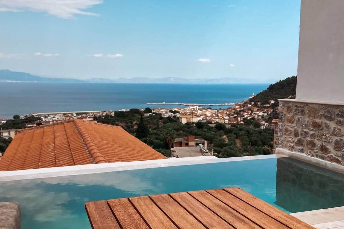 Un espace aménagé au bord de la piscine, avec une table en bois et une vue sur la mer et la ville en arrière-plan.