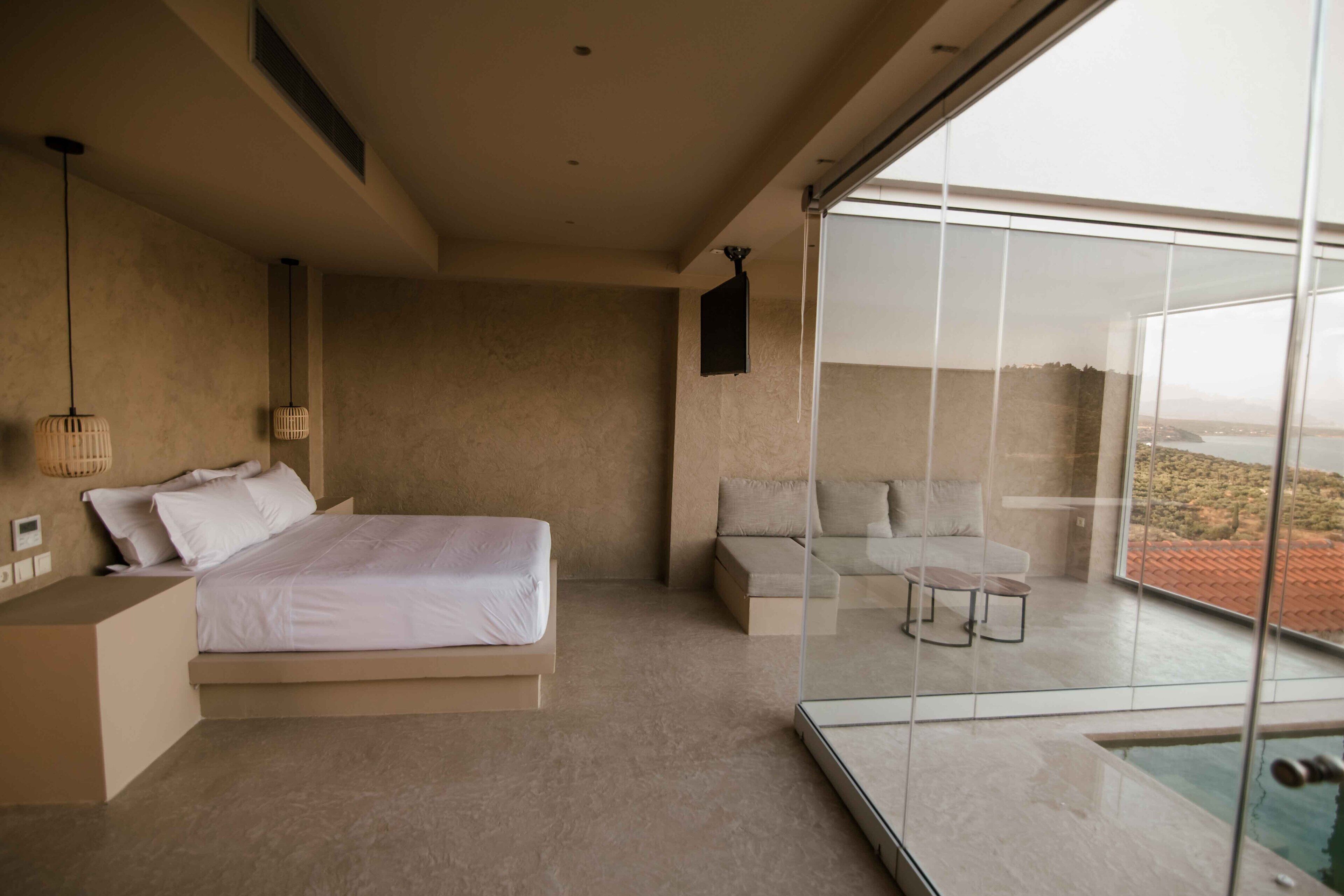A modern bedroom with a large bed, a seating area, and a balcony with a view.