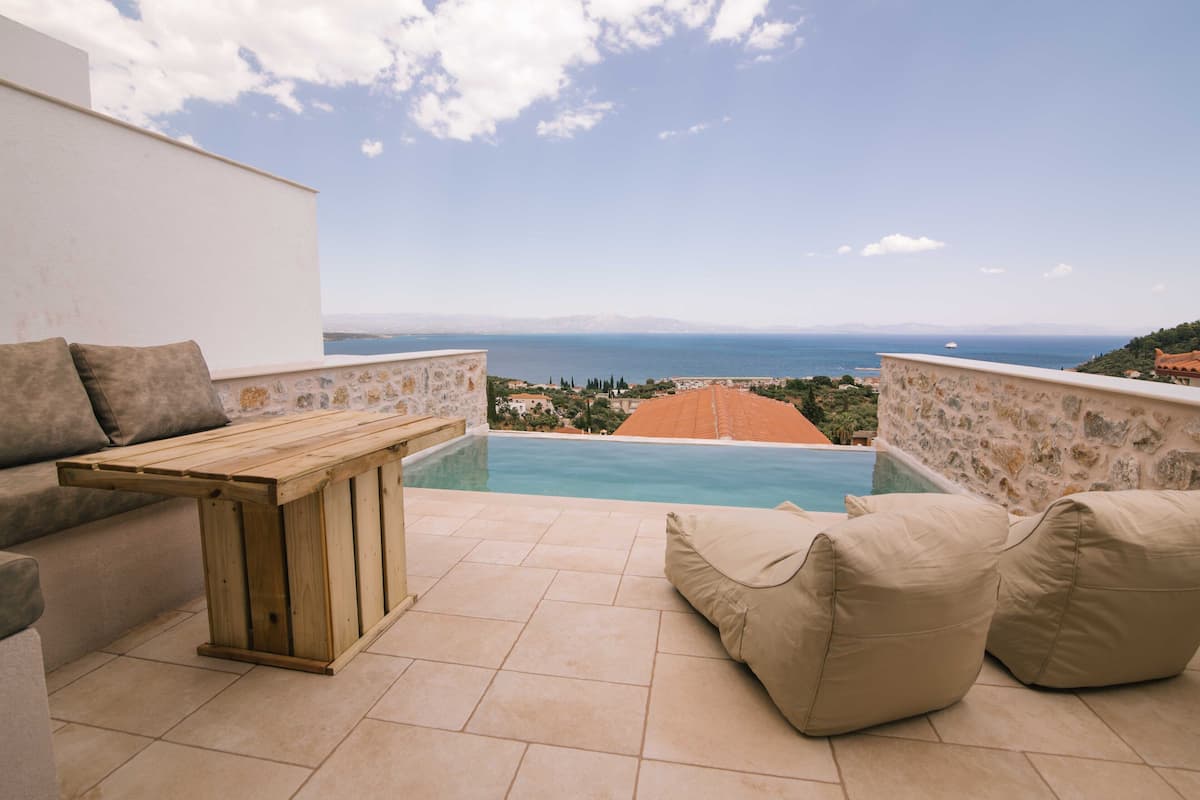 Une terrasse avec une piscine, une table en bois et des coussins de couleur beige.