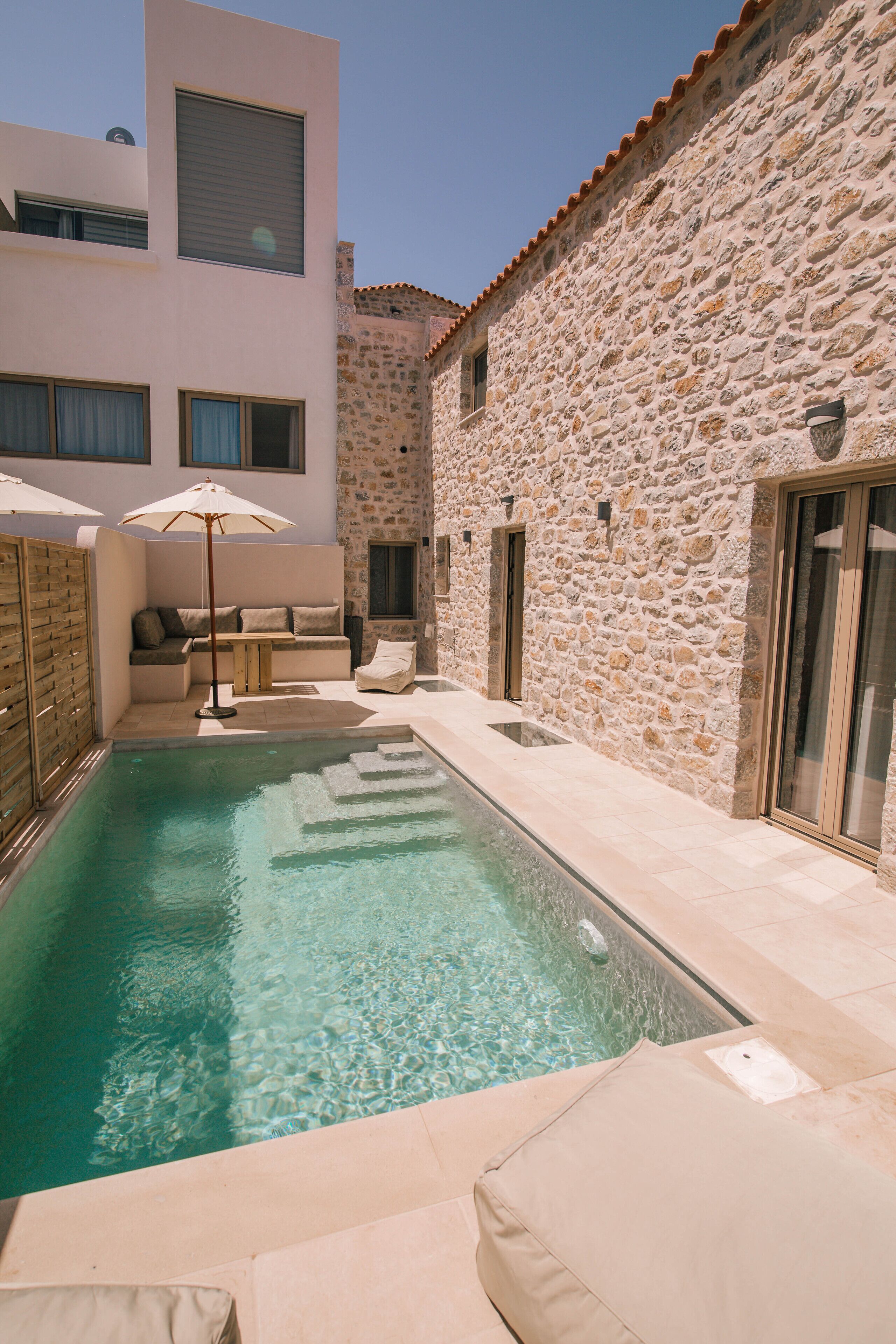 Una piscina con una parete in pietra e un edificio moderno sullo sfondo.