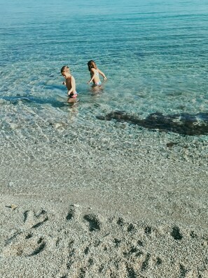 Two children playing in shallow water at a beach with clear visibility to the sea.