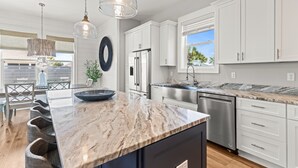 A modern kitchen with white cabinets, a marble countertop, and stainless steel appliances. - Dancing Heron - West End PCB, Pool + Golf Cart 🛺, Sleeps 12 (Panama City Beach)