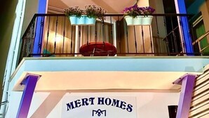 Un edificio de varios pisos con balcones, cada uno decorado con macetas. El edificio tiene un letrero que dice "MERT HOMES".