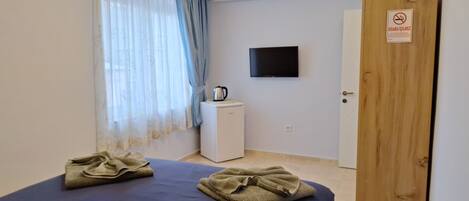 Une petite chambre propre, équipée d’un lit, d’une télévision, d’une machine à café et d’une porte sur laquelle est apposé un panneau « interdiction de fumer ».