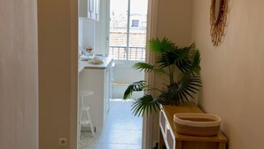 A narrow hallway with a white door leading to a kitchen area. There is a potted plant on a wooden table and a woven basket on a shelf. - URBAN AP4346 By Riviera Holiday Homes (Niza)