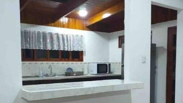 Cozinha com bancada branca, micro-ondas e dois banquinhos de madeira.