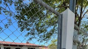Propriedade cercada com um prédio branco, um portão de metal e um abrigo de utilidades.