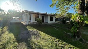 Uma casa térrea com varanda coberta, um pequeno jardim frontal e um carro estacionado na frente.