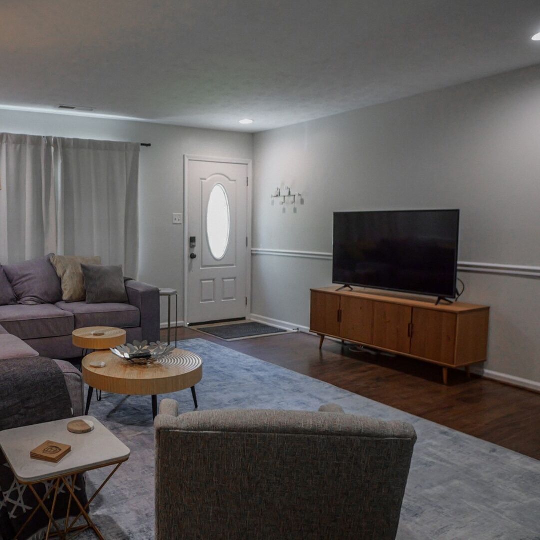 Una sala de estar con un sofá, una mesa de centro, un televisor sobre un mueble de madera y una puerta con espejo.