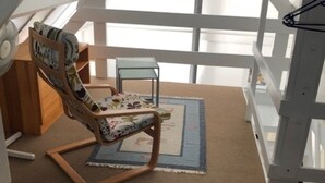 Une pièce mansardée chaleureuse, avec un plafond en pente, un fauteuil à bascule en bois, une petite table et une fenêtre laissant entrer la lumière naturelle.