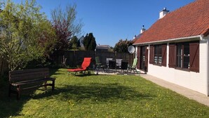 Un jardin avec une pelouse, un banc, un fauteuil de jardin rouge et une table à manger avec des chaises.