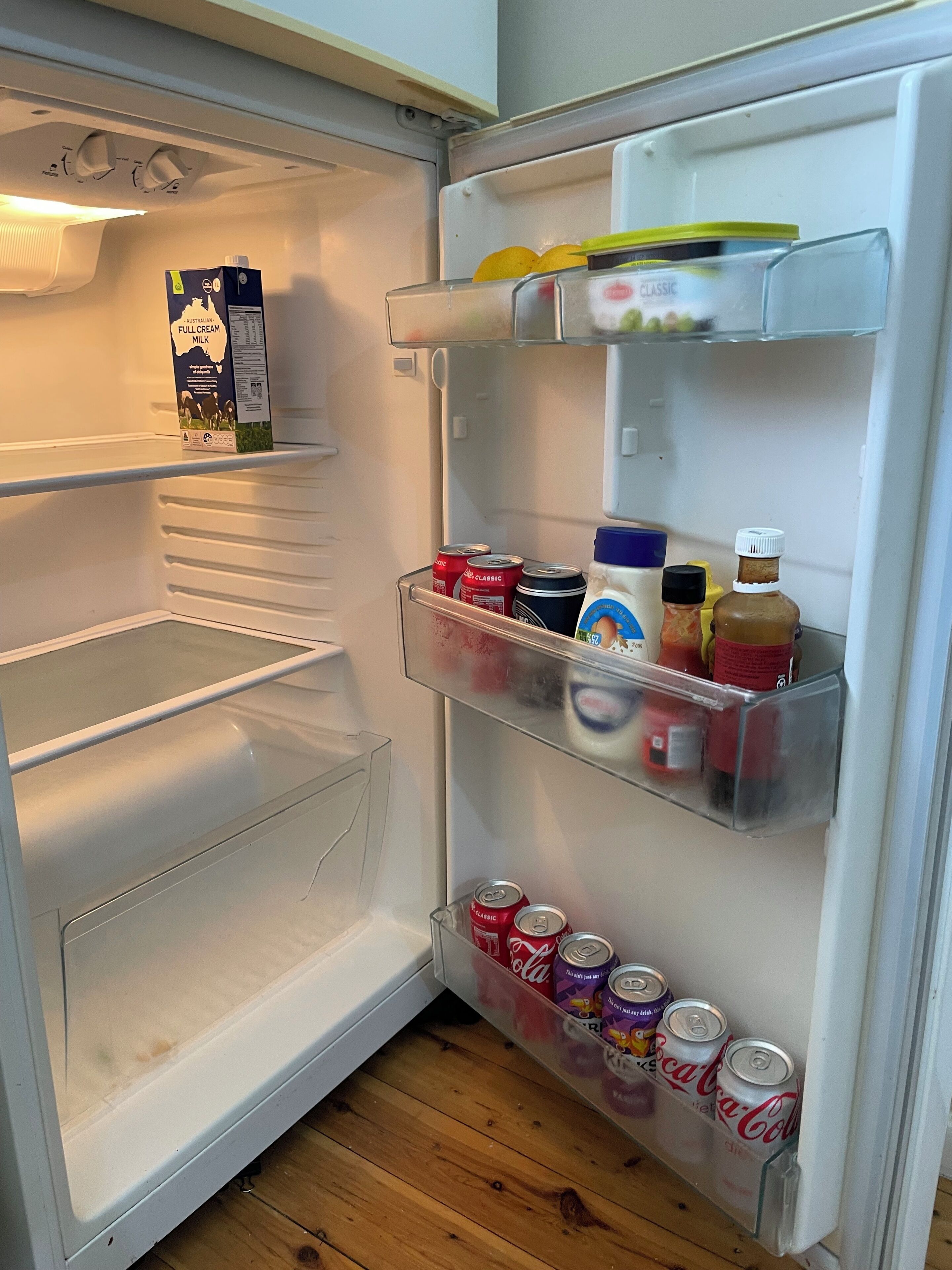 An open refrigerator with shelves containing milk, soda cans, and condiments.
