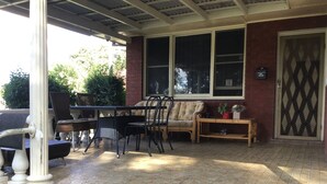 Ein überdachter Patio-Bereich mit Tisch, Stühlen und einer Bank, sowie eine Tür mit dekorativem Muster.