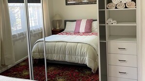 Ein Schlafzimmer mit einem großen Spiegel, einem Bett mit einer rot-weißen Steudecke, einem Nachttisch, einer Lampe, einem Bild an der Wand und einem Schrank mit gefalteten Handtüchern.