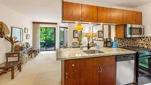 A modern kitchen with wooden cabinets, granite countertops, and stainless steel appliances. - Waikomo Stream Villas 503 – PBAC Membership, Walk to Shops & Ocean (Koloa)