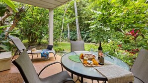 A round glass table set outdoors with a bottle, cheese, and fruit. - Waikomo Stream Villas 503 – PBAC Membership, Walk to Shops & Ocean (Koloa)