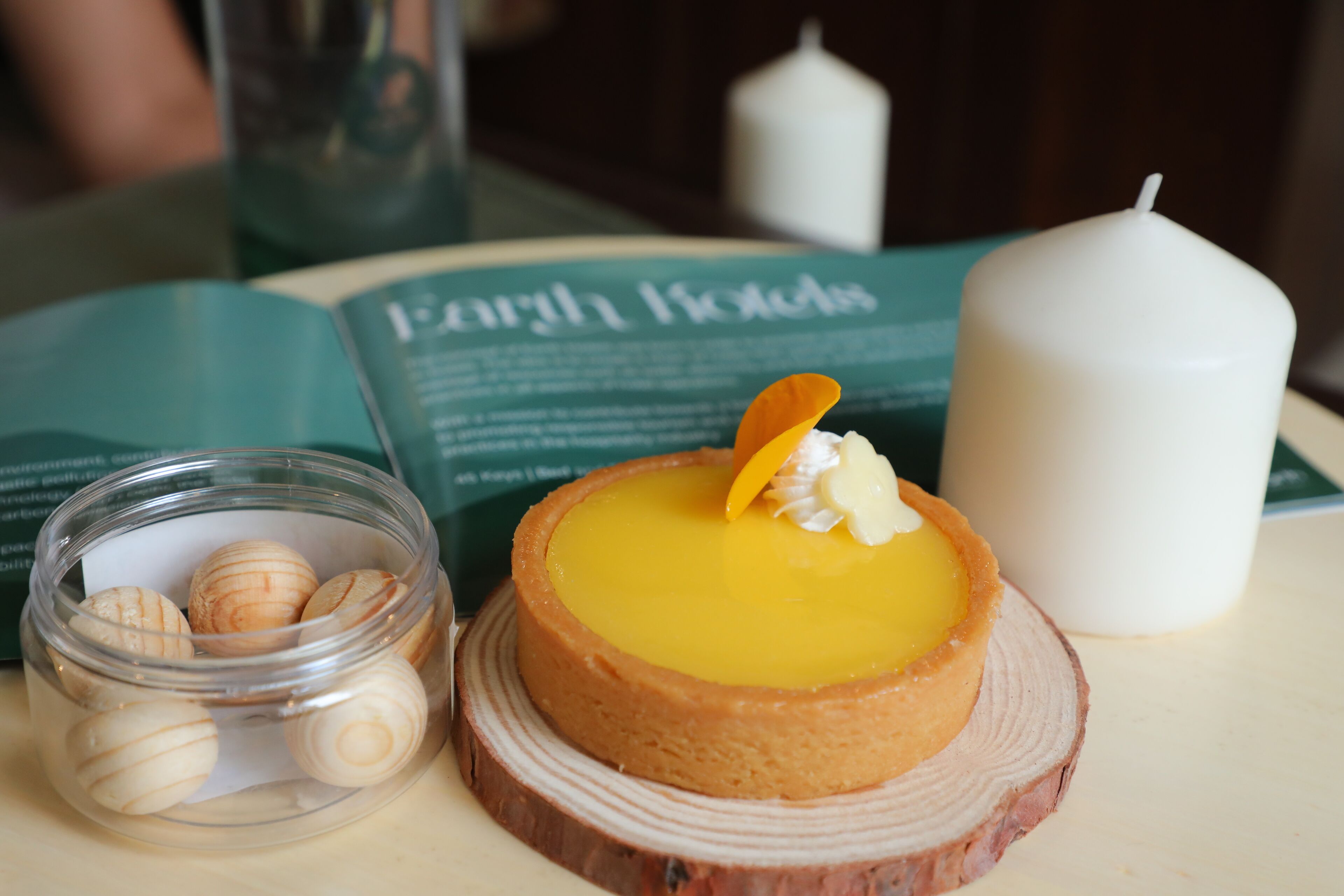 A dessert on a wooden board, a candle, and a book titled "Forthwith Hotels".
