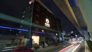Un hotel con un cartello ben visibile, una scalinata che conduce all'ingresso e una strada trafficata con veicoli in movimento.