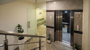 Un interno moderno con una porta in vetro che dà su un'area salotto, una parete in marmo e un ascensore.