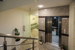Et moderne interiør med en glasdør til et opholdsområde, en marmorvæg og en elevator.