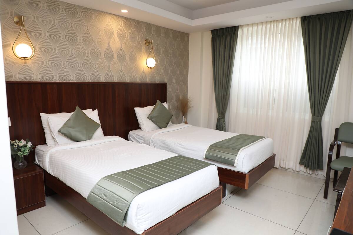 A hotel room with two beds, a wooden headboard, a nightstand with a vase of flowers, and a chair.