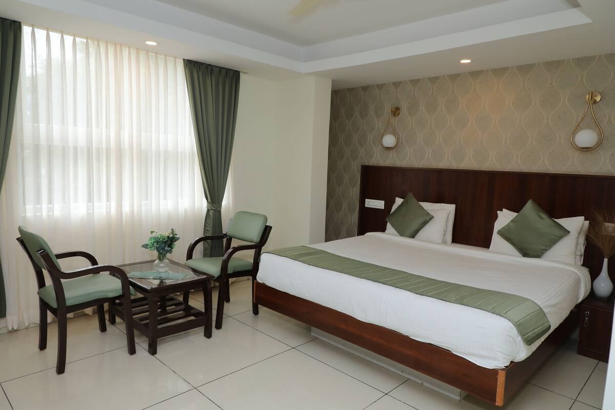 A hotel room with a large bed, two chairs, a small table, and a window with curtains.