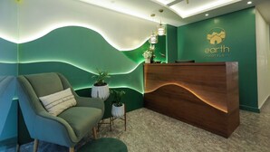 Un'area reception con parete verde, scrivania in legno, divano verde e un piccolo tavolino con piante.