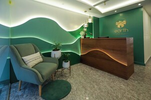 En reception med grøn væg, et træbord til receptionen, en grøn sofa og et lille sofabord med planter.