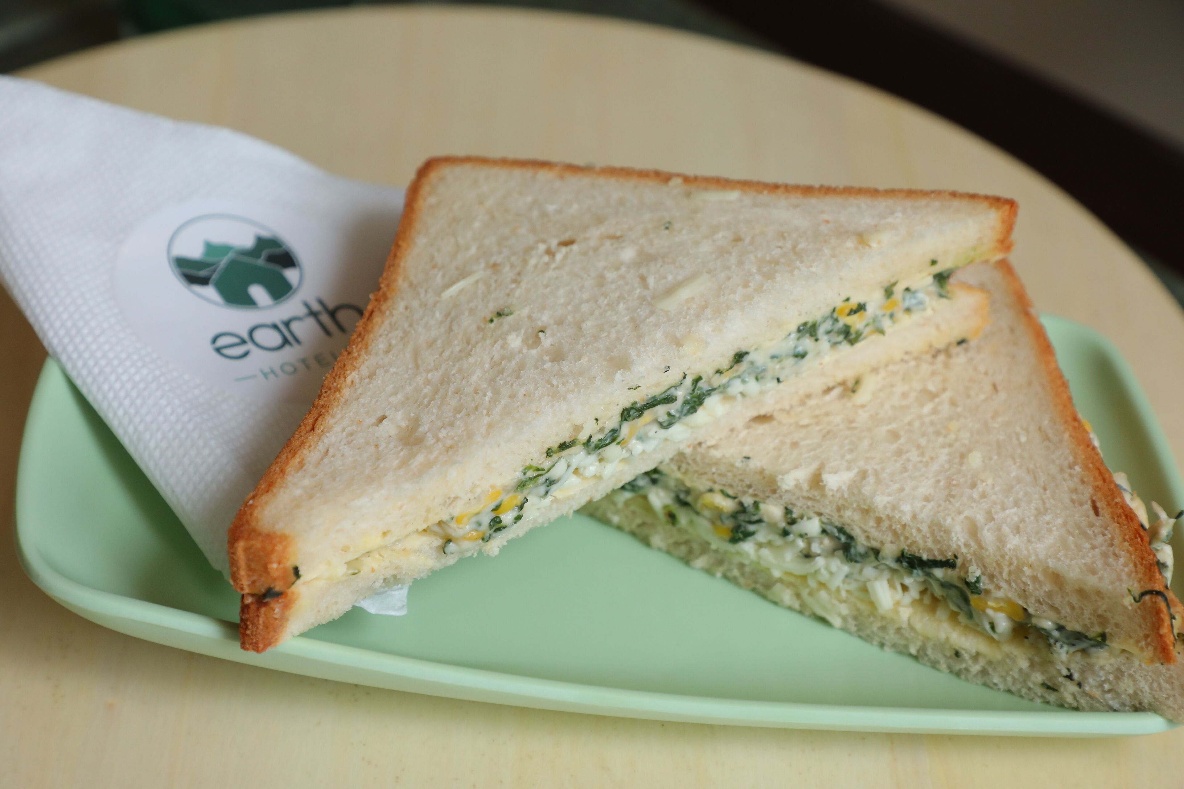 A sandwich on a green plate with a napkin that has a logo.
